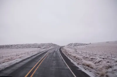 A serene winter road stretches through a snowy landscape, perfect for travel or nature themes.